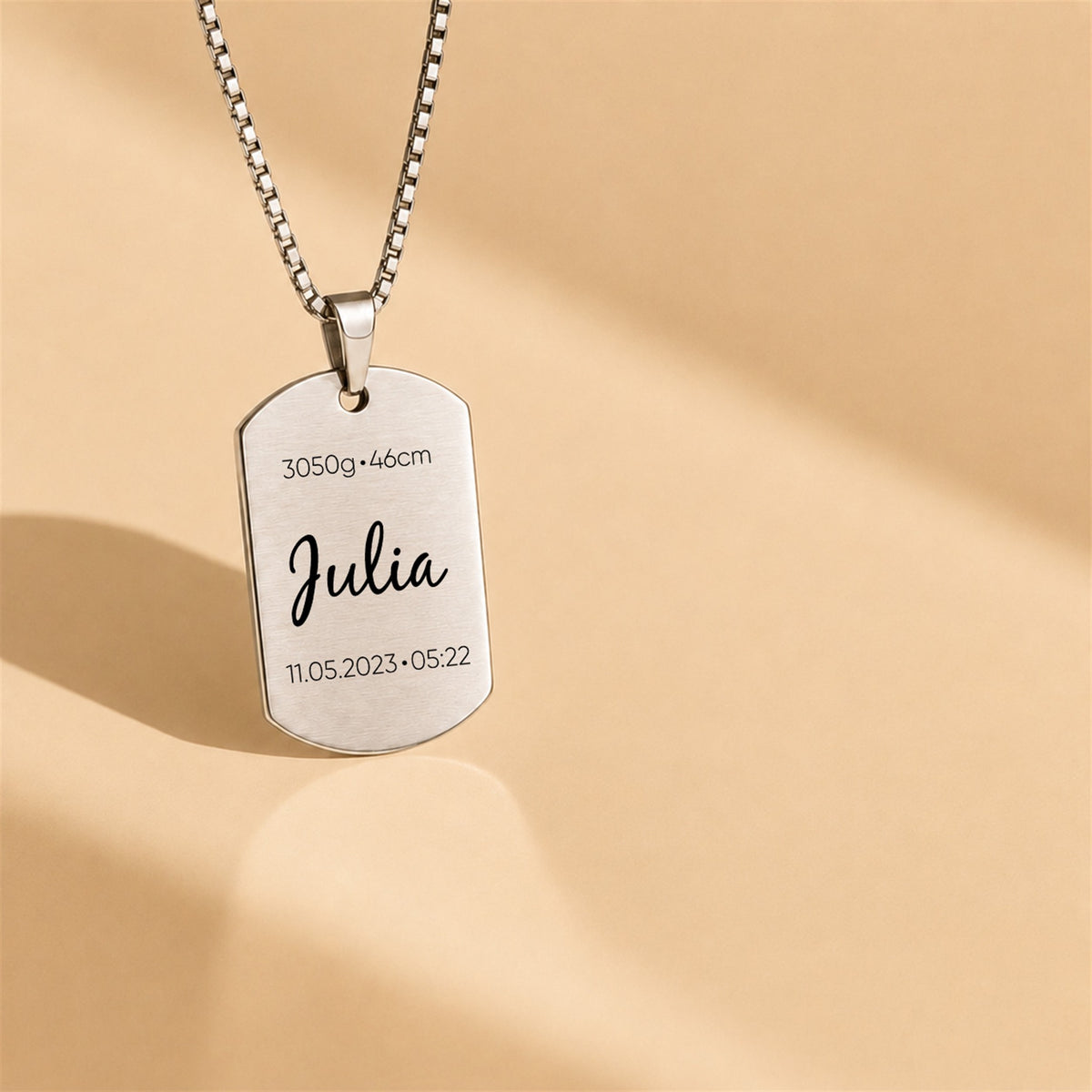 Silver dog tag necklace with engraved name 'Julia' on a beige background